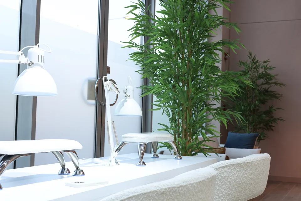 Empty manicure stations beside tall windows and greenery at Beauty Airways